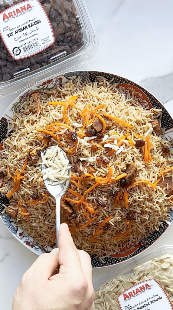 Kabuli palaw in a big plate being topped with carrots, almonds and raisins